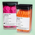 Two dispenser canisters of elastomeric ligature ties in pink and orange